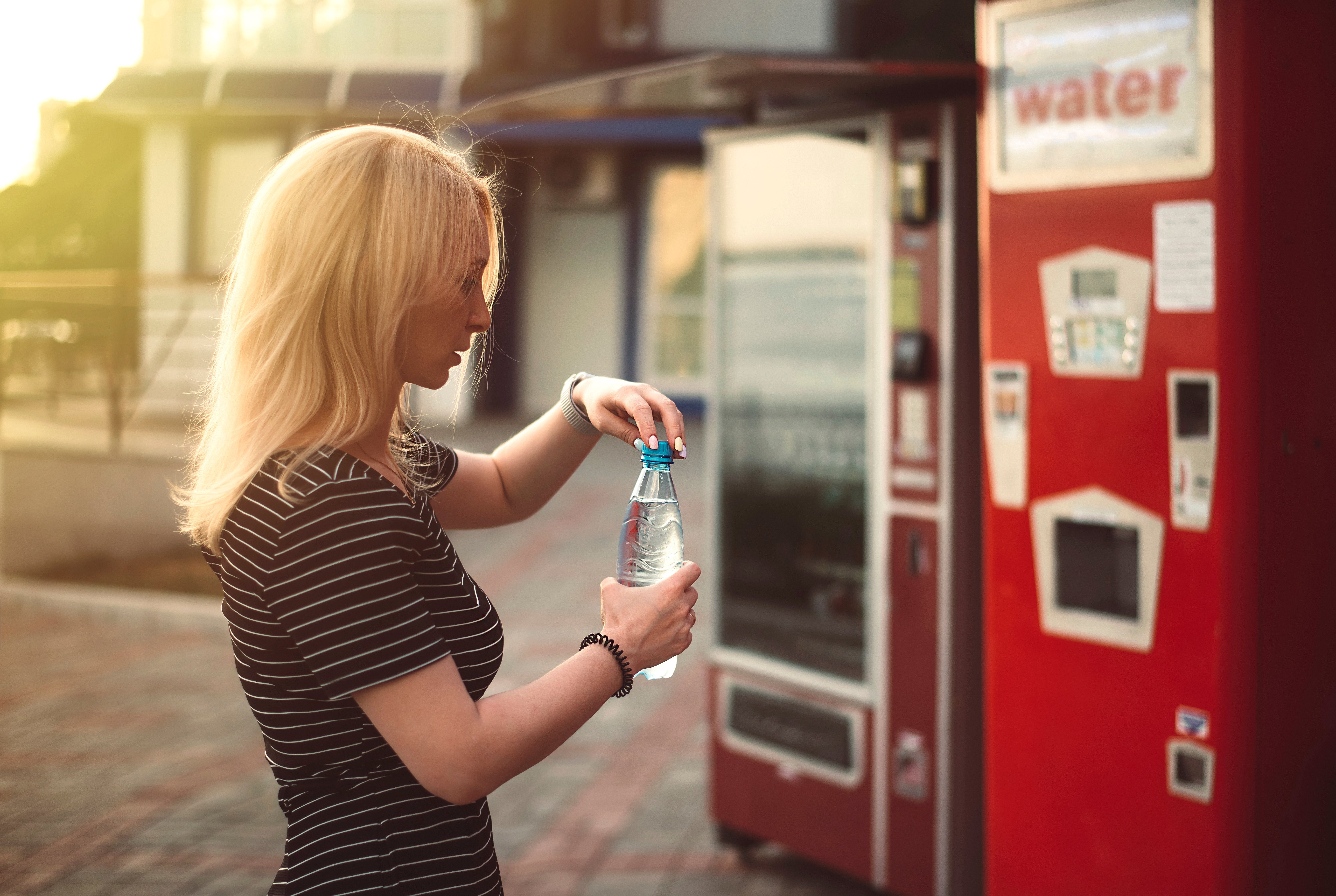 Girl with water in the park on a hot summer day near the vending machines at sunset